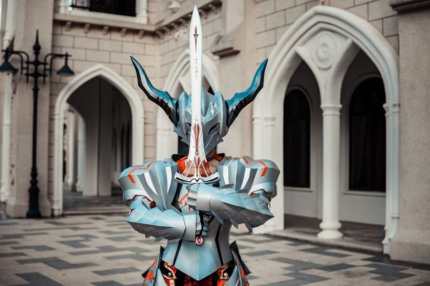Personagem em armadura escura enfrenta uma criatura colossal em campo de batalha ao entardecer, estilo Elden Ring